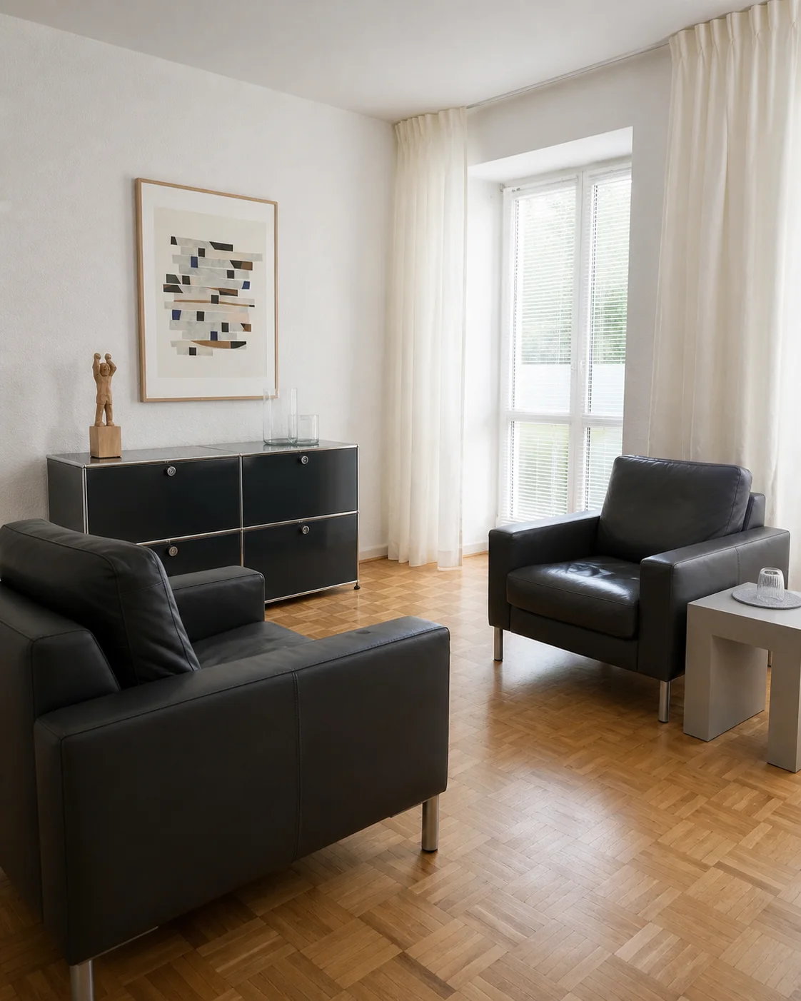 Heller Praxisraum mit zwei anthrazitfarbenen Sesseln, Graphitschrank und Eichenparkett